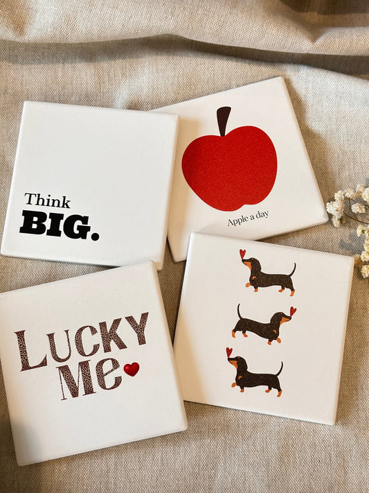 Set of four personalized ceramic dessous de verre featuring natural stone texture with red apple, dachshunds, "Think BIG.