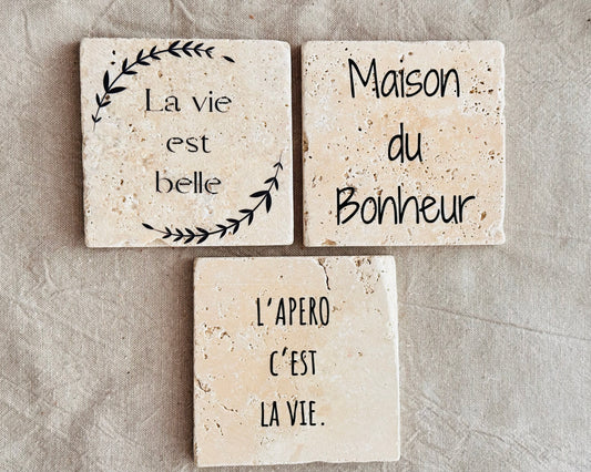 Set of three natural stone dessous de verre with personalized French messages in black ceramic text.